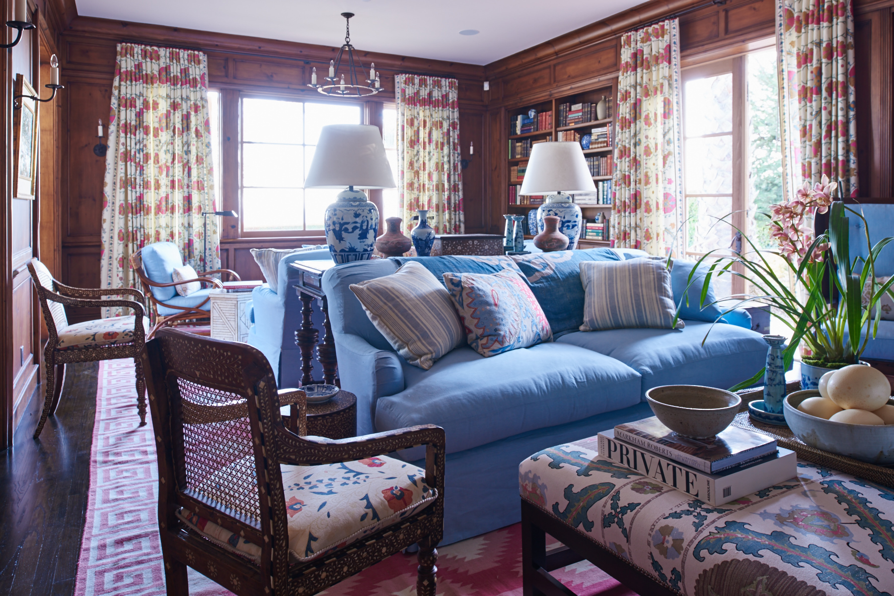 Blue upholstered sofa and chairs with red patterned drapery in the library