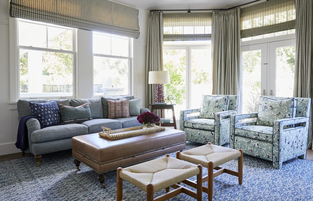 Wide view of living room with herringbone sofa, paisley sitting chairs, checkered drapes, and woven wood shades