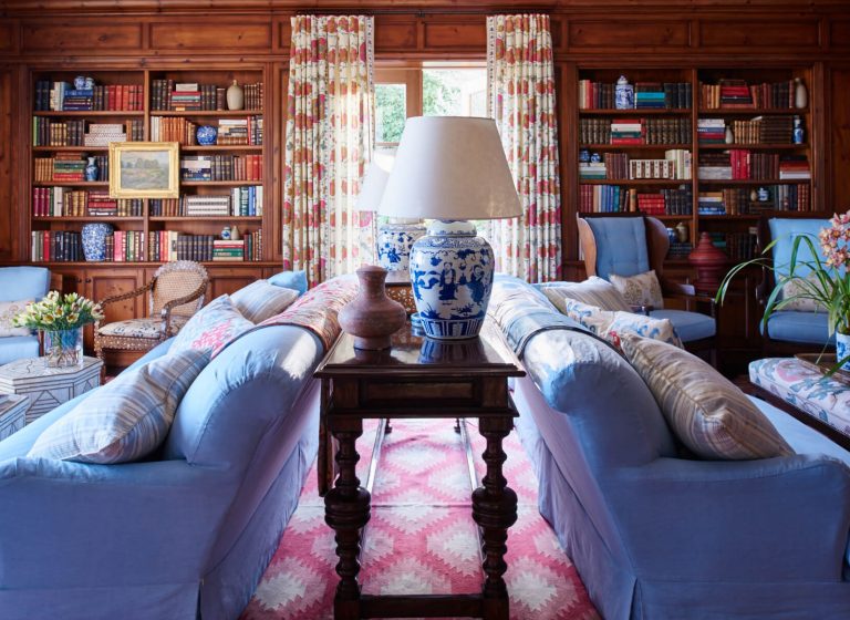 Blue upholstered sofa and chairs with red patterned drapery in the library
